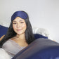 Woman in bed smiling and wearing a blue silk sleep eye mask