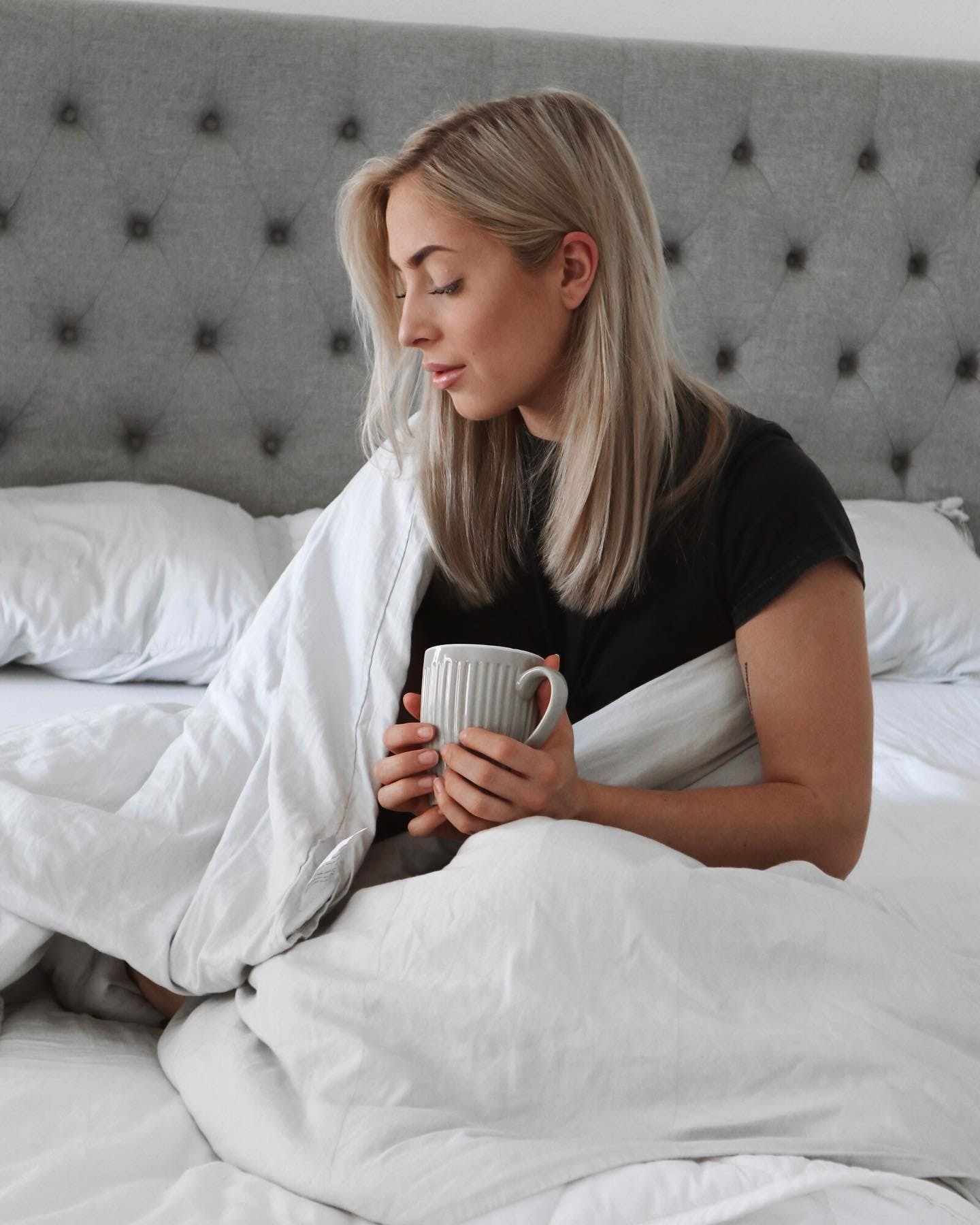 A blonde woman with a hot drink in a duvet containing a weighted blanket