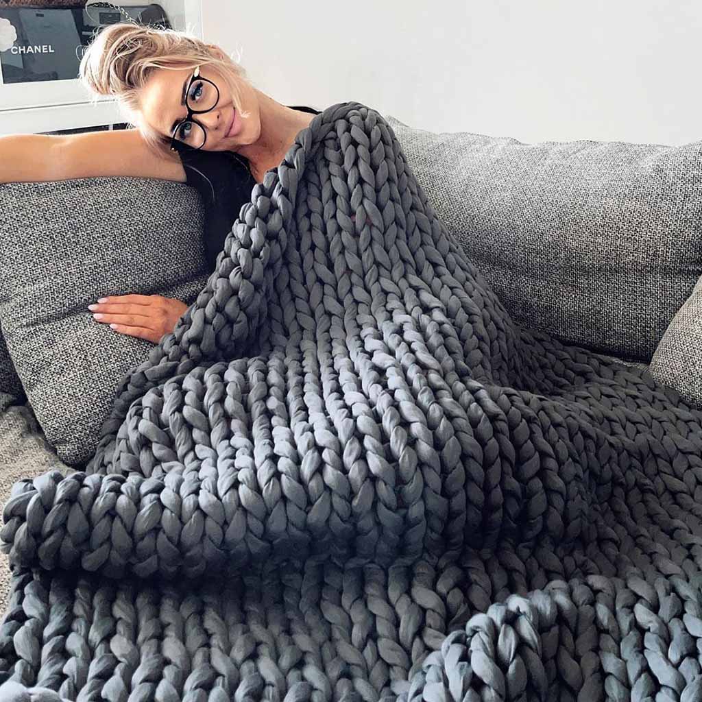 A blonde woman resting with a dark grey knitted blanket