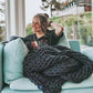 A blonde woman reads a magazine wrapped in her knitted weighted blanket